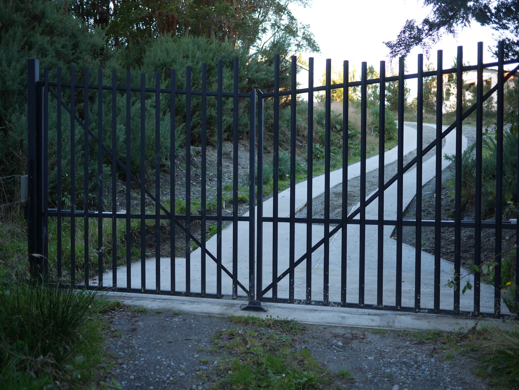 Portón abatible de metal cerrado sobre el acceso de hormigón a una casa en Cihuinco, Chiloé
