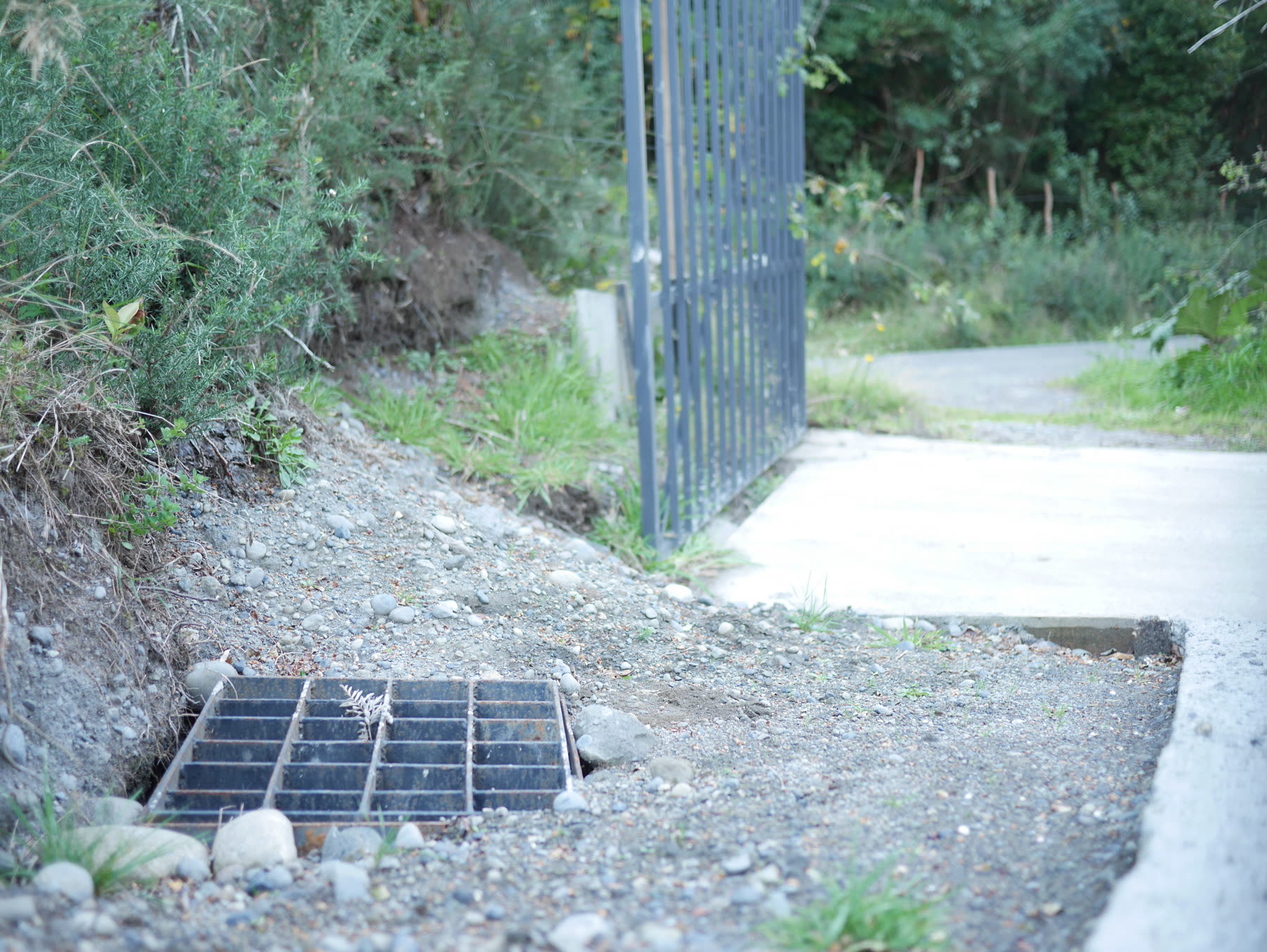 Cámara de aguas con rejilla metálica junto a la base del pilar del portón, en Cihuinco